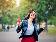 a woman in a red skirt is laughing and holding a cell phone while walking down the street