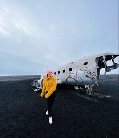 a woman in yellow jacket standing next to an airplane on black sand area with blue sky