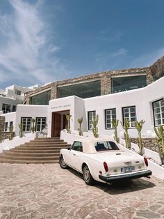 a white car is parked in front of a house with cactus trees and steps leading up to it