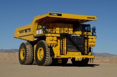 a large yellow dump truck parked on top of a dirt field