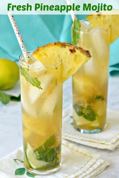 two glasses filled with lemonade and mint on top of a white cloth covered table