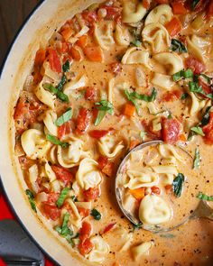 a pot filled with pasta and sauce on top of a red table next to utensils