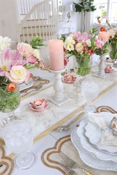 the table is set with pink and white flowers in vases, candles, and plates