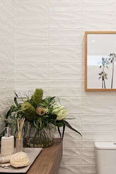 a white toilet sitting next to a wooden table with plants on it and a framed picture