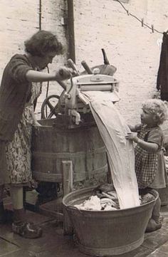 an old black and white photo of a woman washing her child's hands in a bucket