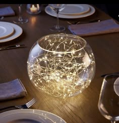 a table set with plates, silverware and lights in a glass bowl on top of it