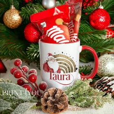 a coffee mug filled with assorted candy and candies next to a christmas tree