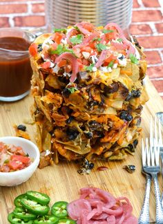 a pile of food sitting on top of a wooden cutting board next to some silverware