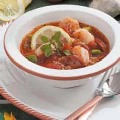 a bowl of soup with shrimp, lemon and basil on the side next to two spoons