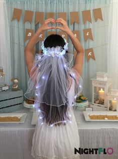 a girl in a white dress is making a heart with her hands at a table