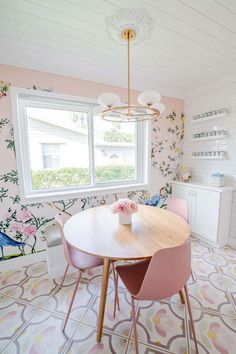 a dining room table with pink chairs in front of a window and wallpaper on the walls