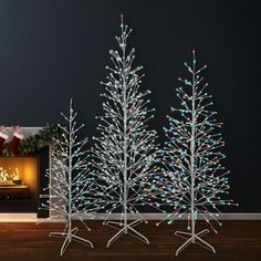 three white christmas trees in front of a fireplace