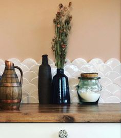 vases and jars are sitting on a shelf in front of a wall with scalloped tiles