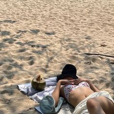 a woman laying on top of a sandy beach next to a palm tree in the sand