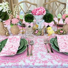 the table is set with pink and green plates, silverware, and flowers in vases