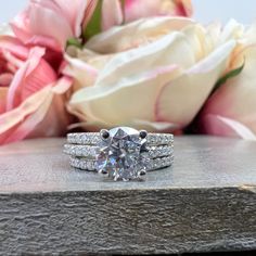 a white diamond ring sitting on top of a wooden table next to pink and white flowers