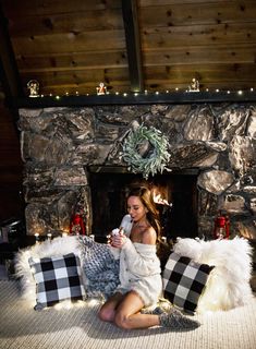 a woman sitting on the floor in front of a fire place holding a cell phone