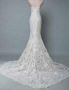 the back of a white wedding dress with an intricate lace pattern and train, on a mannequin