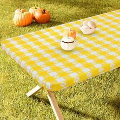 a yellow and white checkered table cloth with two small dishes on it, sitting in the grass next to pumpkins