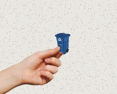 a hand holding a small blue object in it's right hand against a speckled wall