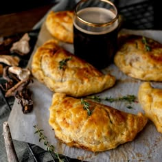 several pastries on a piece of parchment paper with a cup of beer in the background