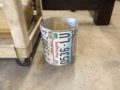 a metal can sitting on the ground next to a wooden table and chair with wheels