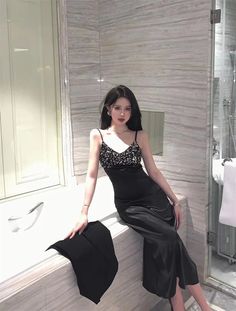 a woman in a black dress is sitting on a ledge next to a bathtub