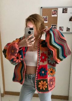 a woman taking a selfie in front of a mirror wearing a colorful crocheted jacket