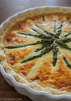 a quiche with asparagus and cheese in a white dish on a wooden table