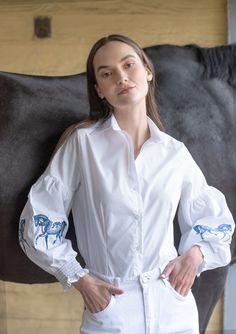 Introducing our new Annie shirt, a classic addition with an equestrian touch. Delicate horse embroidery graces the sleeves of this crisp white button-down, adding a hint of charm. Smocked details on the cuffs enhance its refined appeal, making it a perfect choice for equestrian-inspired looks. With upgraded lantern sleeves, it's both fun and elegant, catering to the modern equestrian enthusiast. Perfect for adding a whimsical touch to your wardrobe or riding ensemble. Don't miss out on the re-launch of the Annie shirt from our equestrian-inspired collection. Shop now to elevate your look with this timeless piece. 97% Cotton 3% Spandex Elegant Embroidered Button-up Blouse, Feminine Button-up Blouse With Floral Embroidery, Spring Embroidered Cuffs Button-up Blouse, Blue Floral Embroidered Button-up Blouse, Summer Sleepwear, Horse Riding Shirts Long Sleeve, Velvet Loafers, White Button Down, Cap Hair