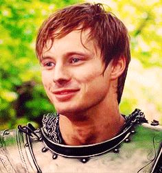 a man in armor is smiling at the camera with trees in the back ground behind him