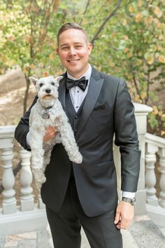 a man in a tuxedo holding a small white dog