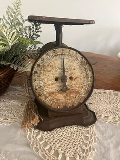 an old time clock sitting on top of a table next to a potted plant