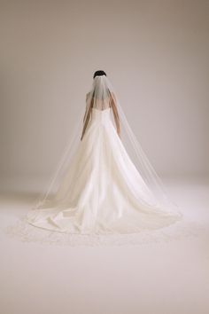 the back of a bride's wedding dress with a veil on her head and shoulders