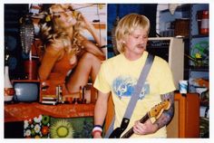 a young man playing an electric guitar in front of a wall with pictures on it