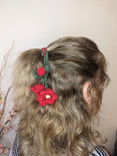 a woman with long hair wearing a crocheted red flower and green leaf headband