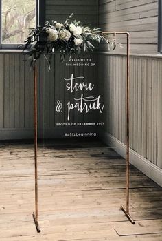 a wedding sign with flowers on it in front of a wooden floor and wall behind it