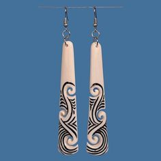 two long white and black earrings hanging from hooks on a blue background with the words,