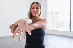 a woman in a black tank top holding her hand out to the side with both hands