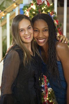 two women standing next to each other in front of a christmas tree with lights on it