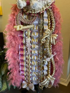 a pink and gold costume with lots of beads on it's chest, sitting next to a potted plant