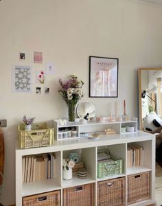 a white shelf filled with lots of books and baskets next to a wall mounted mirror