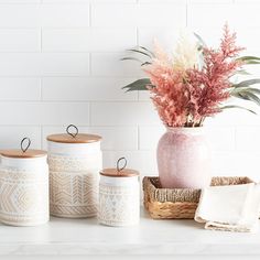 three white jars with pink flowers in them on a table next to a wicker basket