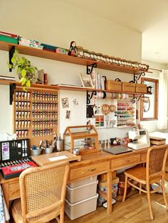 a wooden desk topped with lots of clutter next to two chairs and a window