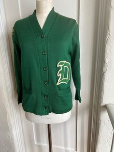 This is a green Albion Knit virgin wool varsity knit cardigan circa 50s/60's. In excellent condition, with no holes snags or stains. Patch on arm is GLS and there is a large "D" patch on front above pockets. There is a faded name printed on label "Tircuit" There is no size label but my guess is small.  Measurements are: Shoulders: 17" Pit to pit: 19" Length: 25" Sleeve length: 21" cuffed, 23" uncuffed Classic Green Wool Cardigan, Green Cotton Sweater With Button Closure, Classic Green Cotton Cardigan, Retro Cotton Cardigan, Retro Cotton Cardigan For College, Green Fitted Wool Cardigan, Vintage Sweater For College In Winter, Vintage College Sweater For Winter, Vintage Winter Sweater For College