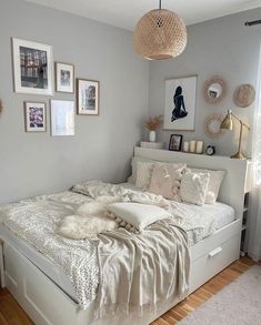 a white bed in a room with pictures on the wall above it and a lamp hanging from the ceiling