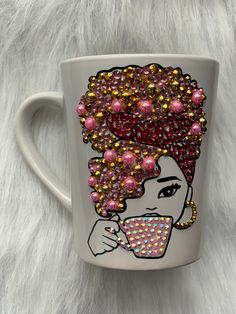 a white coffee cup with pink and gold beaded designs on the side, featuring a woman's face