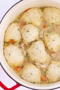 a pot filled with dumplings and vegetables on top of a white countertop next to a red spatula