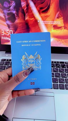 someone is holding up a blue passport in front of a laptop