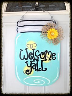 a blue mason jar with a yellow flower on the front and welcome y'all sign above it